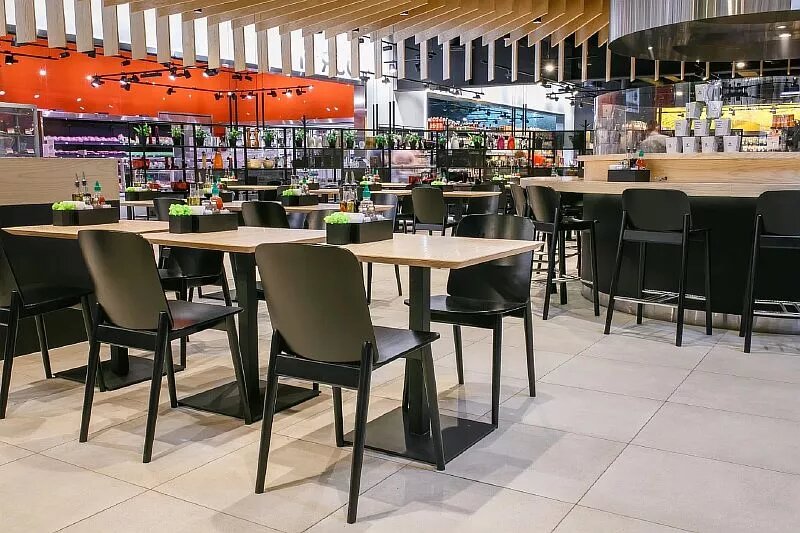 

Несмотря на то, что фудкорты считаются общим пространством, их пространство все чаще подвергается минимальному разделению. Речь не идет о зонировании, а скорее о гибкой, плавающей подсветке. Зачастую посетители после приобретения продукции в одном из кафе стараются сесть за столик напротив него. Обычно так поступает 90% людей. Именно этот момент и подтолкнул владельцев торговых точек уделять больше внимание именно этим зонам, находящимся в 5-8 метрах от прилавков. Описываемая площадь не редко освещается направленными светильниками на шинопроводе, причем каждый ориентируется на определенное место. В итоге достигается идеальная функциональность и эстетичность помещения.

Нужно понимать, что зоны фудкортов должны выгодно отличаться от других уголков торгового центра. При их оформлении в дизайне желательно придерживаться яркости, броскости, выразительности. В конечном итоге это позволит «заманить» публику с тем, чтобы они обратили внимание на выставленные предложения. Общий же комфорт достигается не только за счет использования правильных светильников освещения. Отдельно необходимо уделять внимание и фирменным столикам, стульям, посуде. Успех в этом вопросе состоит из ряда мелочей. Важно сделать все для того, чтобы клиент в заведении общественного питания получил исключительно положительные эмоции, которые могли бы его заставить туда вернуться снова.

Не простой задачей является освещение кафе в районе расположения дальних столиков. Необходимо не просто сделать хорошую подсветку поверхности, а дать человеку понять, какая именно фирма является организатором «банкета». Реализуется поставленная задача окрашиванием устройств освещения в фирменные цвета, нанесением на них логотипов, размещением на плафонах различных предложений, скидок и другой тематической информации. Добавим, что многие элитные фудкорты устанавливают за каждым столиком стилизованные настольные лампы, которые вызывают у посетителя неподдельный интерес.