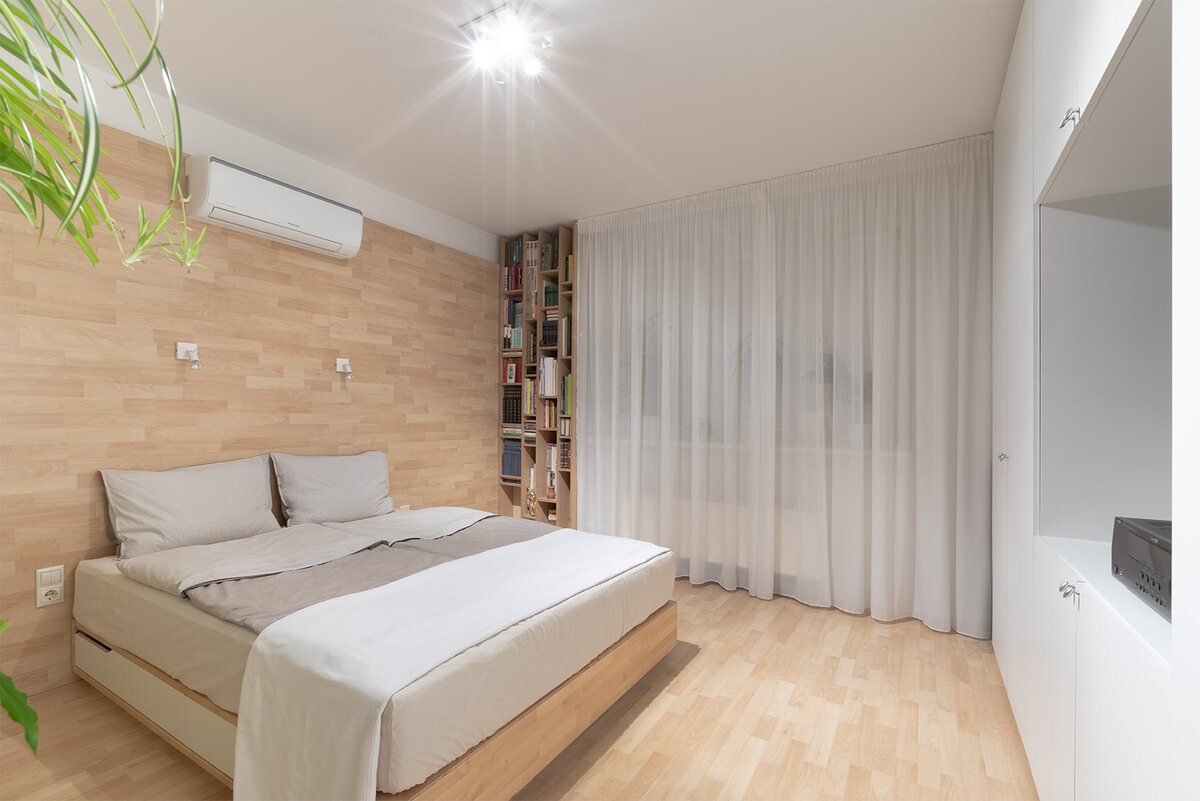 Спальня решена в светлых тонах: в белом и тепло-бежевом цвете. В отделке комнаты использован ламинат (высокоплотная древоволокнистая плита) с фактурой бука. С помощью ламината оформлена акцентная стена-изголовье. *
