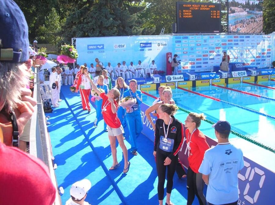 - Всегда интересно знать, каковы были первые шаги чемпиона в спорте?
- Ну, надо начать с того, что я сначала попала не в плавание, а в другой вид. Моя бабушка работала с мамой Ирины Калининой на одном предприятии. Конечно, все ее знали в Пензе, то, что она завоевала золотую олимпийскую медаль, все хотели равняться на такую чемпионку. И у бабушки сразу возникла мечта, чтобы отдать внучку в прыжки в воду. Ирина Владимировна как раз завершила карьеру и стала набирать маленьких детей. И я попала в ее первый набор. Занималась прыжками в воду несколько лет, успехи были на школьном уровне. Но, как выяснилось, я была трусихой, боялась высоты. Когда все детишки бежали на вышку, прыгать «солдатиком» с 7-ми, с 10-ти метров, я шла, держась за перила, такой страх был! Это и стало причиной расставания с прыжками в воду, хотя у меня многое получалось.- И только потом плавание?
- Я просидела дома полгода. Но энергии много, ребенок-то активный. Я, если дома в зал заходила, то обязательно с «колесом», не просто ногами. Пошли смотреть, куда меня могут взять в 8 лет. В художественную гимнастику поздно, на коньки – тоже поздно. Взяли в плавание, хоть ребята и там занимались уже несколько лет, все стили знали. И я стала их догонять. После прыжков физическая подготовка была хорошей, на воде я держалась, просто не знала технику. И, что самое интересное, мне долгое время не давался баттерфляй, тот стиль, который потом у меня стал основным в плавании. Он технически и физически более сложный, так что первые годы я выступала кролем, брассом, на спине. Но с годами, в результате огромного труда, баттерфляй стал выравниваться. Я почувствовала гребок, как тянуться вперед, стала прогрессировать. А потом на соревнованиях тренеры смотрели, что лучше получается. Именно на соревнованиях, потому что и на тренировке можно неплохо проплыть. Но на соревнованиях, когда настраиваешься, когда ты на адреналине, выясняется, кто ты – спринтер, стайер или середняк, какой вид у тебя лучше. И так на протяжении нескольких лет. Если ты плывешь баттерфляем по нормативу заслуженного мастера спорта, а «спину» - по кандидату, тут уже выбора быть не может!- А потом победы на различных стартах, звание чемпионки России и, как следствие, попадание на Олимпиаду. Можно ли сравнить Сидней-2000, Афины-2004 и Пекин-2008?
- Мало быть чемпионкой страны, надо было проплыть по нормативу, попасть в годовой рейтинг. У меня все это совпало, и я поехала на Олимпиаду. Впечатление от Олимпиады ни с чем не сравнишь, это особенный праздник. Конечно, там есть соревновательный дух, но атмосфера теплая, дружеская. Как и было задумано в древние времена: должны закончиться войны. И честь страны защищают не армии, а представители в различных видах спорта, и все это на доброй, честной волне.- Но это вне бассейна. А в бассейне, наверно, все по-другому?
- В бассейне кипят страсти, энергия! Выходишь, а там трибуны полные! В Сиднее была надежда на попадание в финал. Я проплыла по лучшему времени оба заплыва, и на предварительном этапе, и в полуфинале. Но даже этих секунд не хватило, другие были лучше готовы. Перед следующей Олимпиадой, в 2004 году я выиграла чемпионат Европы. По длинной воде, на дистанции 50 метров. Но, к сожалению, «полтинника» не Олимпиаде нет! (смеется) Естественно, было воодушевление, и на вторых для себя Играх я опять улучшила результат. Но все равно этого было мало, если уж улучшать, то качественно, более значительно. И на второй Олимпиаде я очень расстроилась, что не смогла себя реализовать. После полуфинала было чувство, что я могла еще быстрее. Недовосстановилась, что ли?- Не было мысли закончить со спортом?
- Нет, такой мысли не было. Если бы я ухудшила секунды, если был бы откат, тогда, может быть. Но у меня постоянно шел прогресс, значит, это не предел возможностей! Мне было 24 года, и я поставила себе цель попасть на третью Олимпиаду. Поехала, и снова показала лучшие секунды. А еще у нас была сильная эстафета, и на нее делалась ставка, что мы сможем быть в «призах» Но заняли мы 5-е место. Конечно, это достойный результат, но наши результаты (эстафету, кроме Натальи Сутягиной, плыли Анастасия Зуева, Юлия Ефимова и Анастасия Аксенова – прим. ред.) позволяли быть третьими. Вот так не доплыла я до медали, осталась недосказанность… После Олимпиады поняла, что сил продолжать нет, больше моральных, чем физических. Тем более, возраст подошел, нужна семья, дети. И я сказала себе: «Хватит!»- Как дался переход к обычной жизни?
- Первый год вообще к бассейну не подходила. Зато сейчас плаваю каждый день. За час до работы прихожу и плаваю. Все-таки потянуло обратно (смеется). Тем более, ехать никуда не надо, после того, как дети выросли, устроилась в СШОР водных видов спорта, курирую отделение прыжков в воду. Дети тоже продолжают спортивные традиции. Дочь Диана занимается художественной гимнастикой, а сын Дамир – самбо и прыжками в воду.- Год получился сложным для всех спортсменов. Прыгуны – не исключение?
- Конечно, пандемия помешала тренировкам. Но дети и тренеры работали дома, тем более, что акробатика в прыжках в воду имеет большое значение. Тренировки проводились согласно расписанию он-лайн, дети получали задания, высылали видеоотчеты. Главные потери в подготовке понесли «вышечники». На вышке желательно перерывов не делать, потом ее тяжело «собрать», да и страх может закрасться. Но вроде бы дети восстановились, и сейчас ждут поездки на международные соревнования