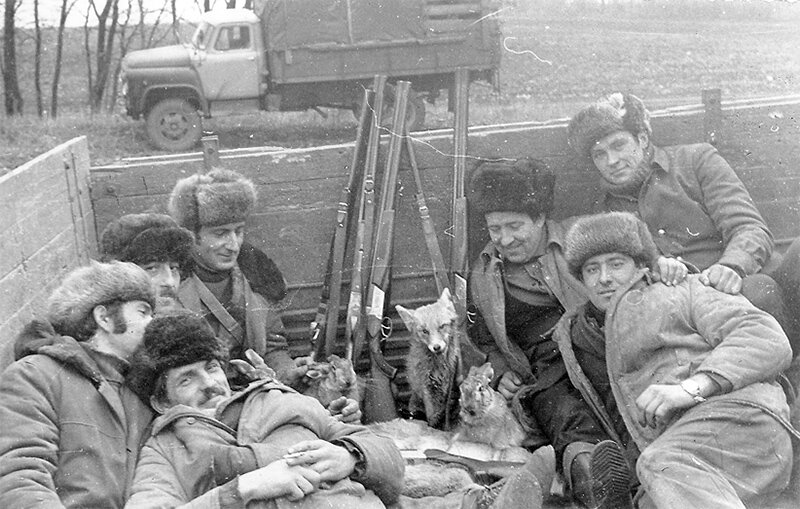 Личный транспорт был не у всех, а на охоту надо было как-то добираться... На заднем плане грузовик ГАЗ-53. Скорее всего конец 70-х или начало 80-х годов XX века. На головах модные в то время шапки, среди ружей, составленных вместе, видны две вертикалки ТОЗ-34 не в самом дешевом исполнении, с гравировкой — компания собралась не самая простая. Охотились на зайцев, попутно взяли лису. Охота удалась!