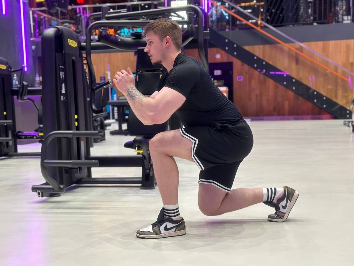 На фотографии тренер Дмитрий показывает упражнение "Выпады" 