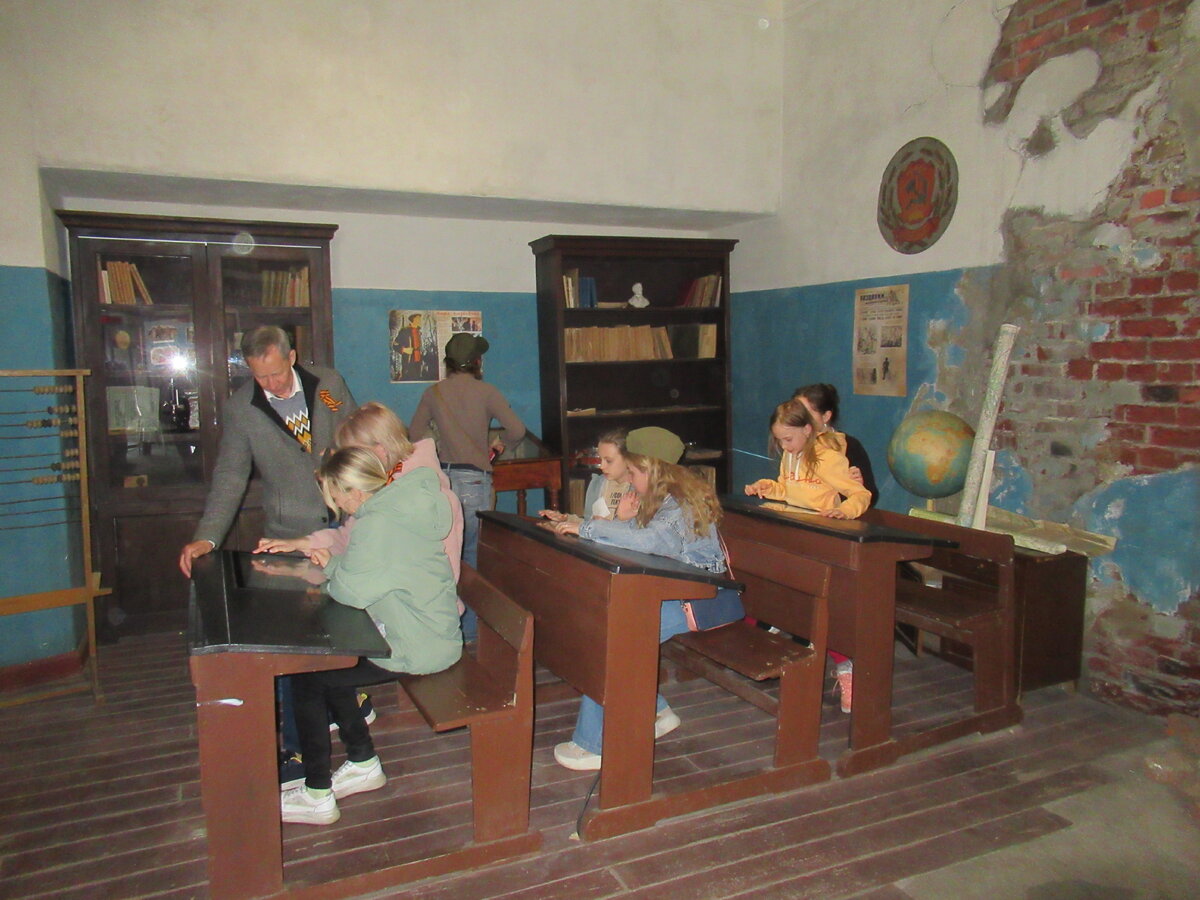 Школьный класс, конечно, его кусочек, парт всего три, когда в классе их было намного больше. В парты вставлены какие-то мониторы, что там не смотрел, так как парты были заняты, очевидно, какая-то информация по школе того периода. Также можно видеть антураж - шкафы тех лет, глобус, герб РСФСР, счеты, плакаты