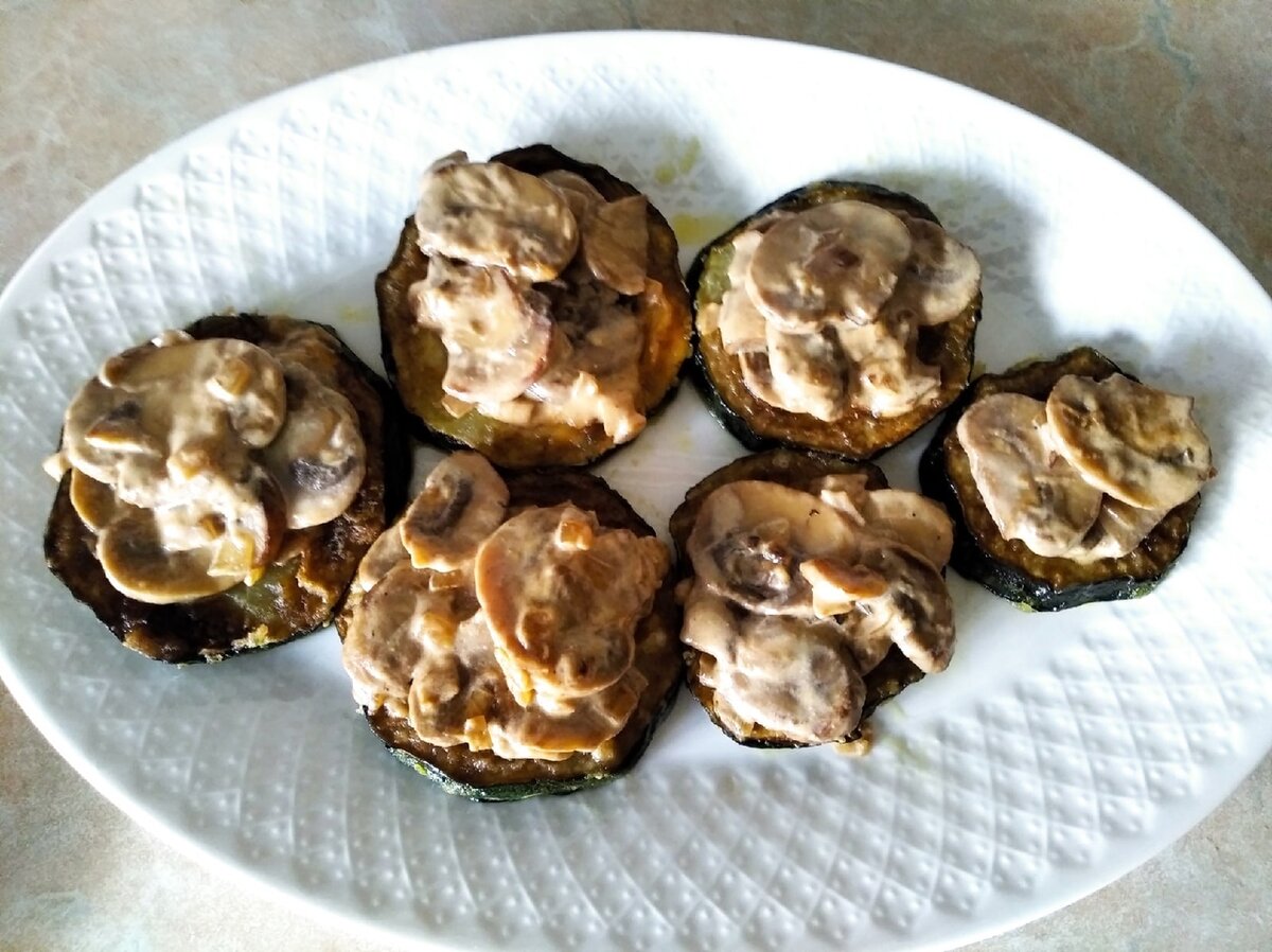 На блюдо уложите кружки обжаренных кабачков и баклажан, сверху положите горку грибов