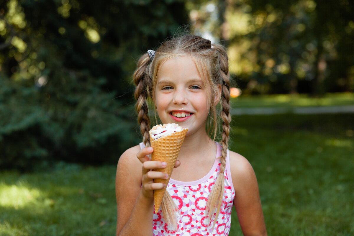 Х ест. Маленькая девочка ест мороженое. Веселая девочка ест\. Девочка ест мороженое в парке. Девочка кушает с мороженым.