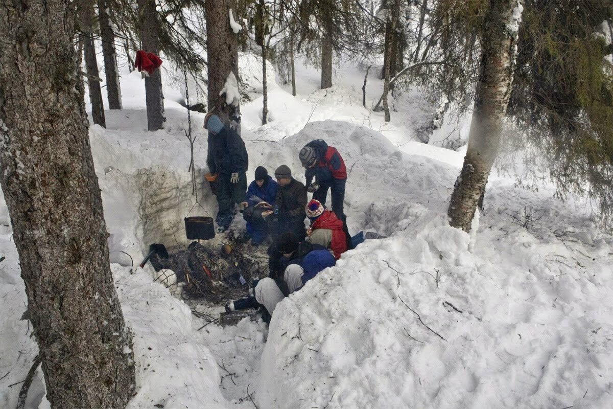 Примерно так выглядит оборудование костра в зимнем лесу. Для защиты от ветра в снегу роют яму до самой земли и расчищают пространство вокруг для размещения людей.  