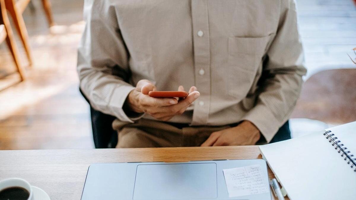    Мужчина сидит перед ноутбуком и держит телефон в руке:pexels.com