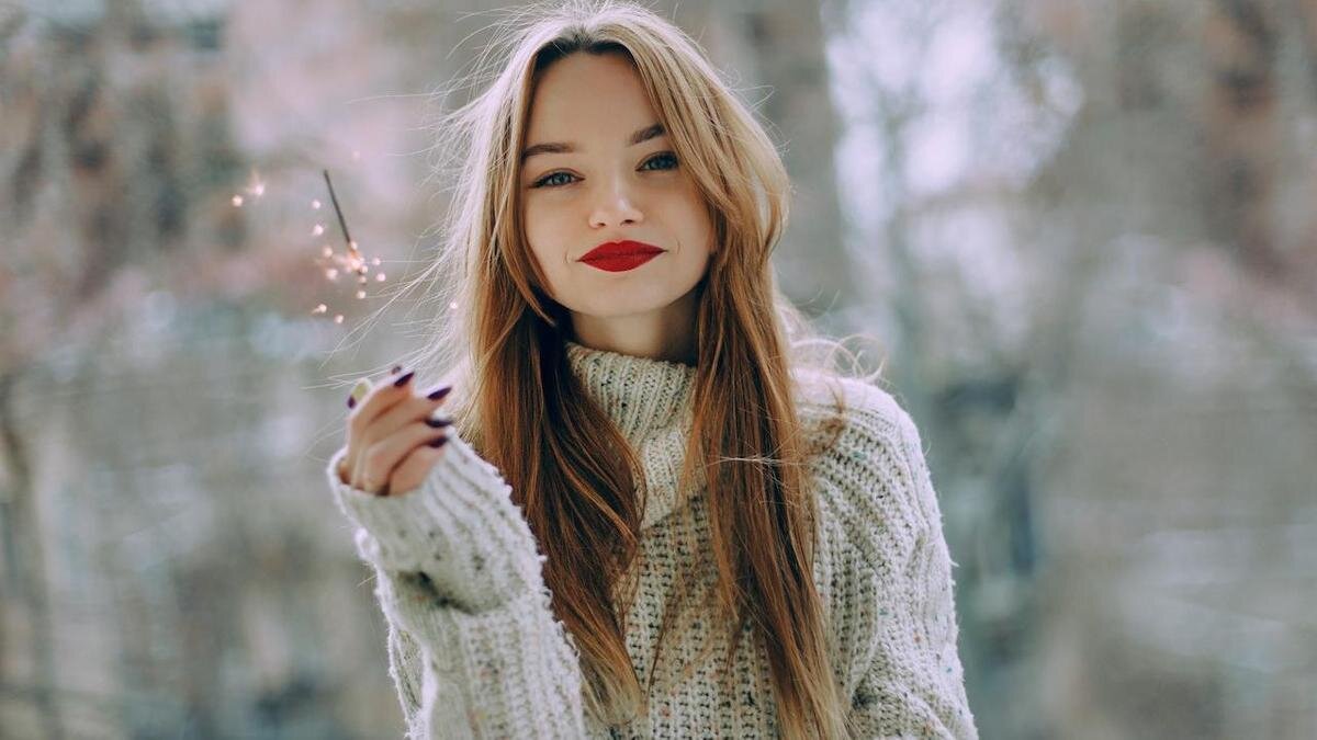    Девушка с длинными волосами и яркой помадой на губах держит в руке бенгальский огонек:Pexels