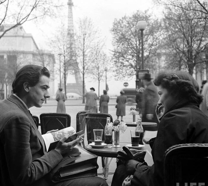 Рекламный плакат: Пара сидит в кафе у Эйфелевой башни, попивая Coca-Cola.