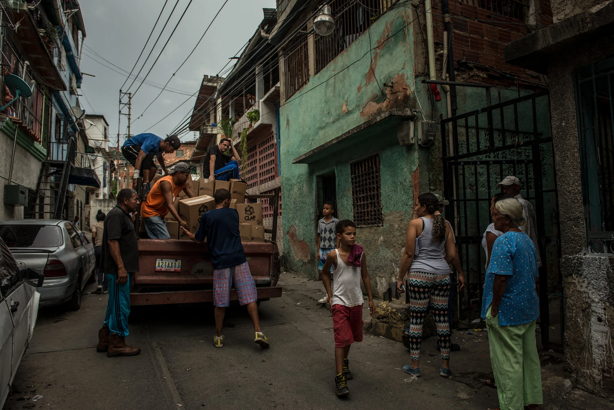 Жители Петаре (большой трущобы на окраине Каракаса) доставляют продовольственные ящики с продуктами, выданные правительством. Меридит Кохут для Нью-Йорк Таймс