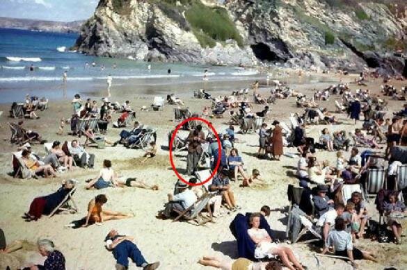 Стюарт Хамфрис занимается колоризацией и реставрацией старых фотографий. Закончив очередной заказ, он выложил результат в социальную сеть, чтобы узнать у пользователей, что за пляж изображен на снимке. Пользователи, однако, помогать в этом британскому фоторедактору не стали. Все дело в том, что их вниманием завладело кое-что другое. 
Дело в том, что среди многочисленных посетителей пляжа они увидели загадочного мужчину. Тот, несмотря на, судя по всему, жаркую погоду, одет достаточно тепло, в отличие от остальных людей поблизости. Но это не самое удивительно. Мужчина смотрит на свои сложенные перед самым лицом руки так, будто у него там самый настоящий современный смартфон. Именно такую догадку выдвинул один из посетителей страницы Стюарта Хамфриса в Twitter. Многие мистификатора поддержали.
