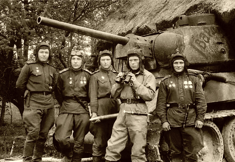 Групповой портрет экипажа танка Т-34 с именем собственным «Гвардия» 2-го батальона 63-й гвардейской Челябинской танковой бригады на Украине. Слева направо: командир танка лейтенант А.В. Додонов, стрелок-радист старшина Александр Порфирьевич Марченко (1913—1944), заряжающий Н.И. Мельниченко, командир батальона П.В. Чирков, механик-водитель старшина Федор Павлович Сурков (1913—1971). Экипажу танка под командованием лейтенанта А. В. Додонова было приказано пробиться к центру города и водрузить красное знамя на ратуше во Львове. Машиной управлял механик-водитель старшина Ф. П. Сурков. Меткий огонь по врагу вел башенный стрелок И. И. Мельниченко. Радист — старшина А. П. Марченко, неплохо знавший город, указывал путь. Действуя решительно, танк «Гвардия», поддерживаемый своим подразделением, прорвался к самому подъезду ратуши. Марченко вместе с группой автоматчиков, перебив вражескую охрану, ворвался в здание, поднялся на башню и водрузил на ней алый стяг. За 6 дней боев в городе экипаж уничтожил более 100 вражеских солдат и офицеров и сжег 8 танков противника. Гитлеровцам удалось подбить танк Т-34 «Гвардия». В жестоком бою с врагом погибли А.В. Додонов и А.П. Марченко, тяжело ранены Сурков и Мельниченко. Старшина Ф. П. Сурков за выдающийся подвиг удостоился звания Героя Советского Союза, остальные члены экипажа были награждены орденами. Звание Героя Советского Союза было присвоено командиру 63-й гвардейской танковой бригады полковнику М. Г. Фомичеву. Снимок сделан перед началом Львовской операции.