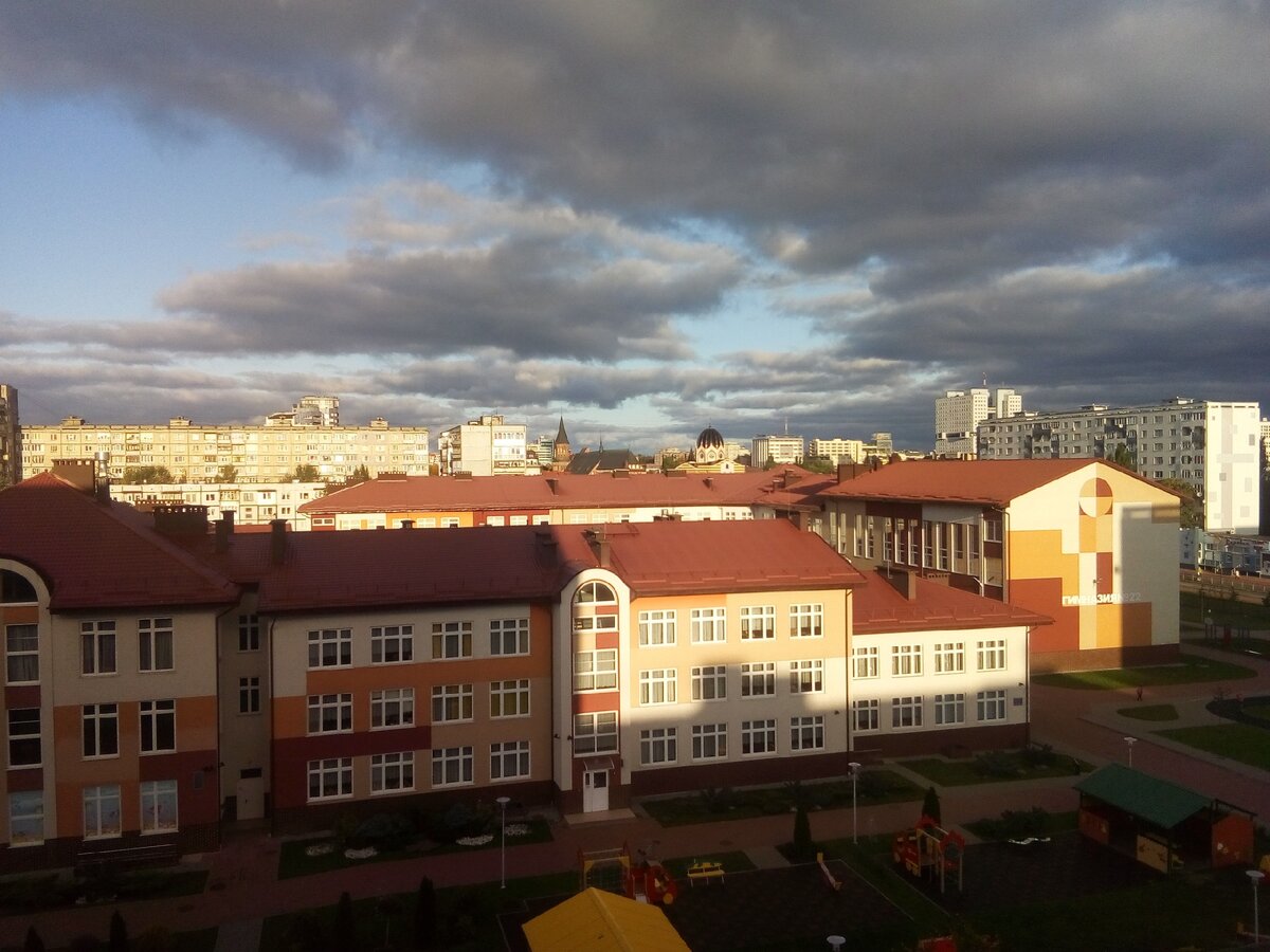 Это вид из окна. Садик. И торец школы. В нём бассейн. Нужно обойти вот это всё, тогда будет вход в школу. Видите, как тень разделила стену, на которой написано слово «гимназия», почти пополам? На дорожке почти на границе тени можно разглядеть Вику