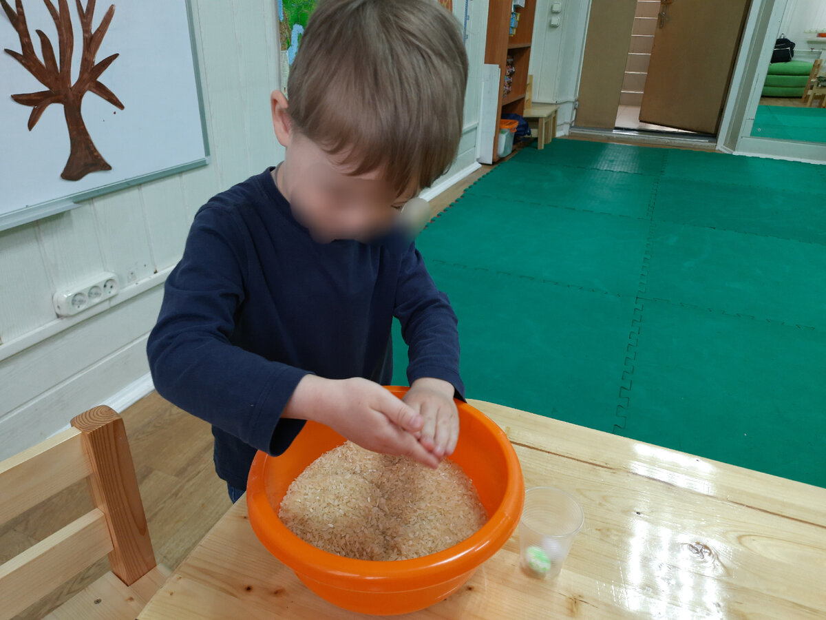 Ищет в тазике с рисом маленькие яйца и складывает их в стаканчик.