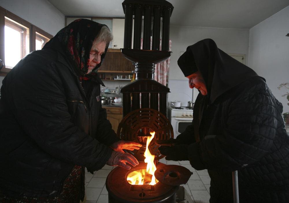 Монахиня и посетитель пытаются согреться возле дровяной печи в монастыре недалеко от столицы Болгарии Софии. Фото AP/Петар Петров.