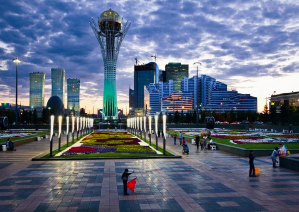 97-метровый Байтерек, возвышающийся над центральным проспектом Астаны, светится зеленым на фоне покрытого облаками вечернего неба. Фото: Герд Людвиг