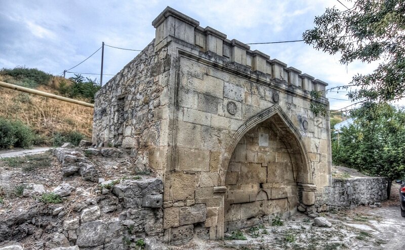 средневековое сооружение, украшенное резьбой — изображением солнца в центре, звезд по бокам и надписью с годом постройки