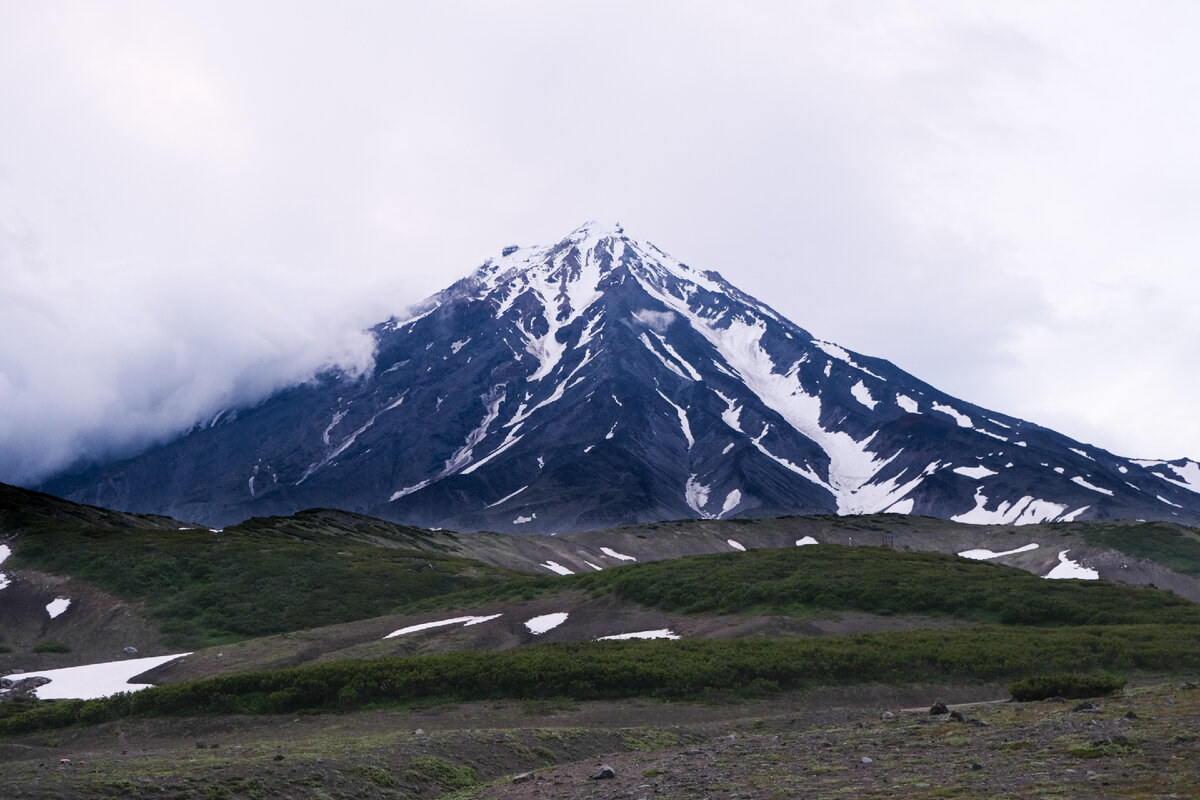 Утро нас встретило хмуро. Прогноз был плохой - низкая облачность и сильные порывы ветра. Наши гиды до последнего решали - идти или остаться внизу. Было принято решения на подъем. Надежда была в том, что когда начнем подниматься, то погода возможно станет лучше и мы сможем подняться на вершину. Эти надежды были не лишены основания. Ветер, то нагонял облака, то обнажал вершину Корякского вулкана. Лишний раз показывая, что прогнозы погоды на Камчатке непредсказуемы. Все может поменяться в любую минуту. 