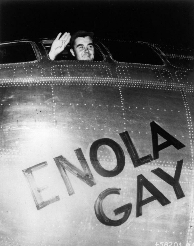 Пилот полковник Пол В. Тайббетс машет рукой из кабины своего бомбардировщика на базе, расположенной на острове Тиниан, 6 августа 1945 года, перед вылетом, целью которого являлось сбросить первую в истории атомную бомбу на Хиросиму, Япония. За день до этого Тиббетс назвал летающую крепость В-29 «Энолой Гей» в честь своей матери.  
