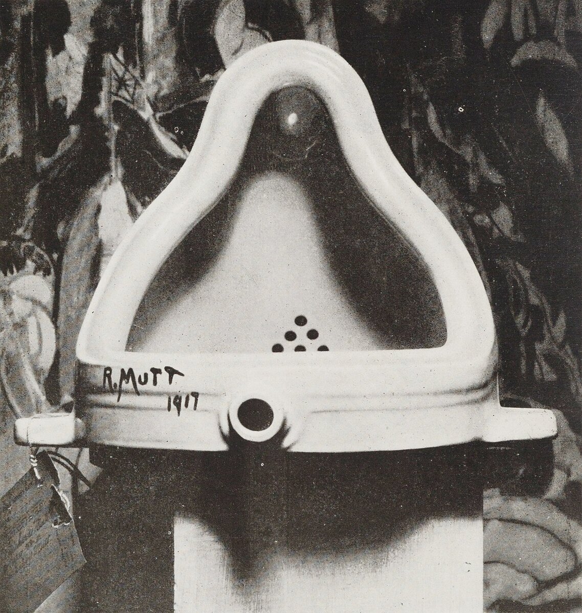 Марсель Дюшан "Фонтан", 1917. Фотография оригинала работы Дюшана, сделанная Альфредом Стиглицем, в качестве фона была выбрана картина Хартли Марсдена "Войны".