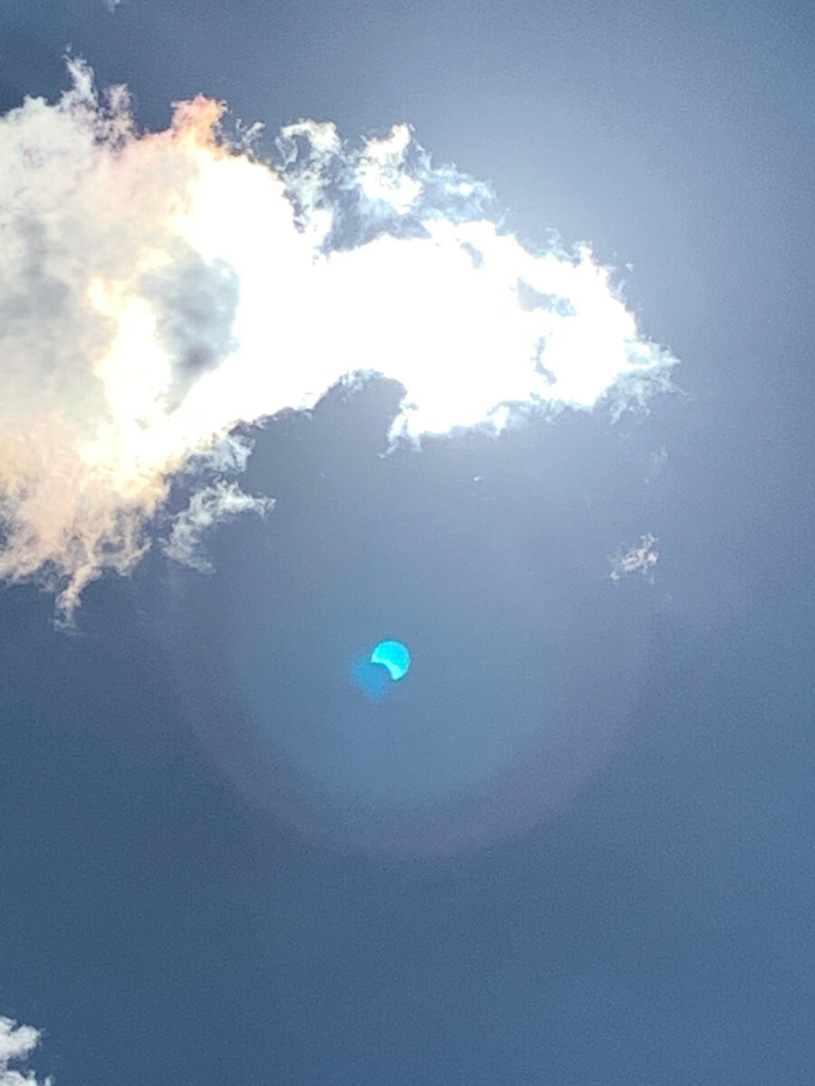 Солнце чуть скрыто за облаками, фото засвечено, но на блике видно частное солнечное затмение.