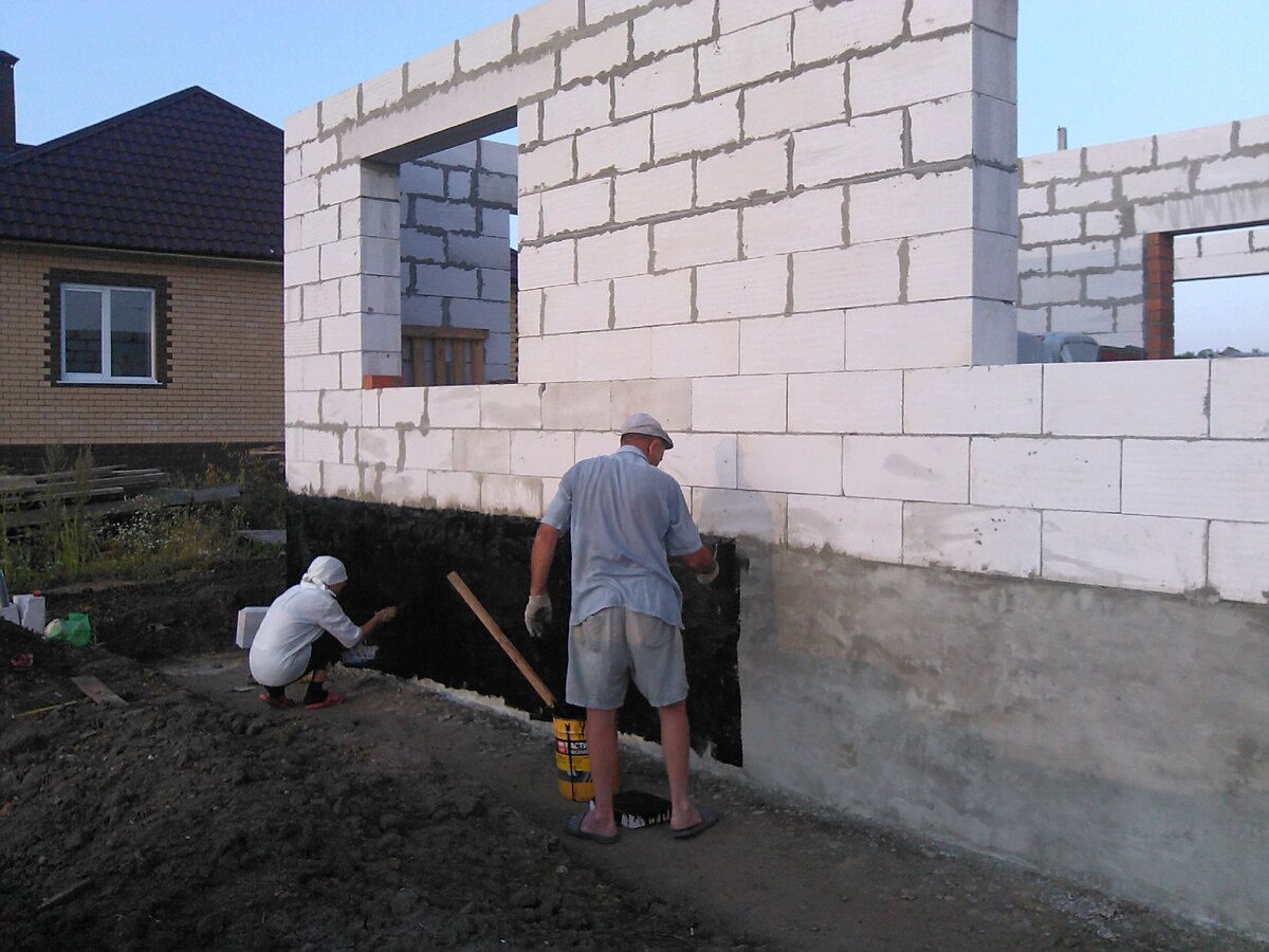 На фото видно, что по периметру дома снят плодородный слой грунта и сделан уклон от дома. Родители помогают с гидроизоляцией. @ Горбунов Сергей
