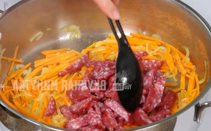 1. Обжариваем измельченную луковицу при среднем огне на растительном масле, готовим до прозрачности. Добавляем натертую или нарезанную соломкой морковку, несколько минут. Затем добавляем колбасу, нарезанную ломтиками. Добавляем шинкованную капусту (половину), солим, перчим. Вторую половину капусты выкладываем в кастрюлю и обжариваем на высоком огне 3-4 минуты.