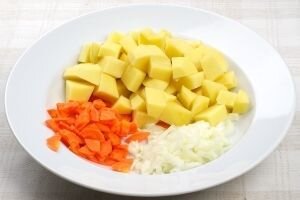    Очистите от кожицы картофель, морковь и лук. Затем все тщательно промойте под струей проточной воды. Далее нарежьте средними кубиками картофель и мелкими репчатый лук. Морковь нарежьте кружочками, каждый из которых поделите еще на четыре части.   