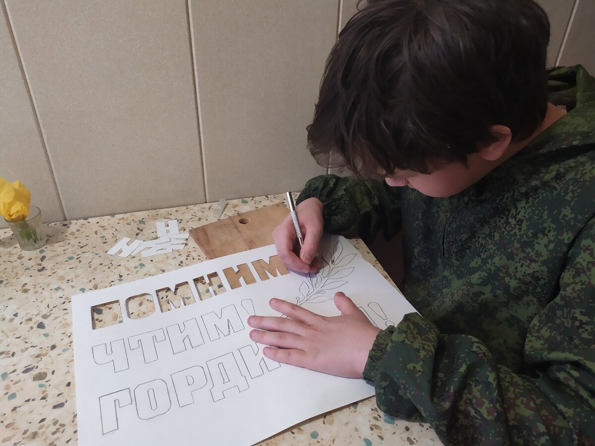 Сын вырезает трафарет ножом.