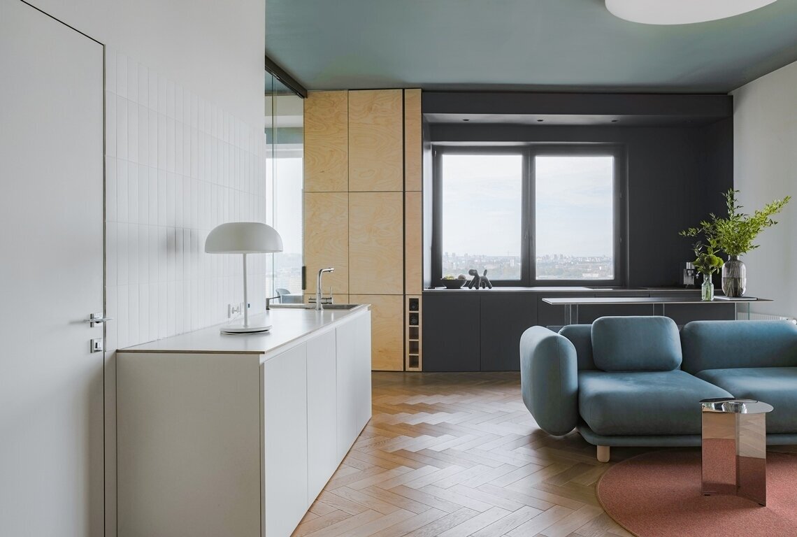 Для стен использовали преимущественно белую краску. Отдельные участки и потолок выкрасили в серо-голубой, зрительно создав продолжение неба в интерьере. Квартира располагается на 22 этаже, откуда открывается захватывающий вид на город.