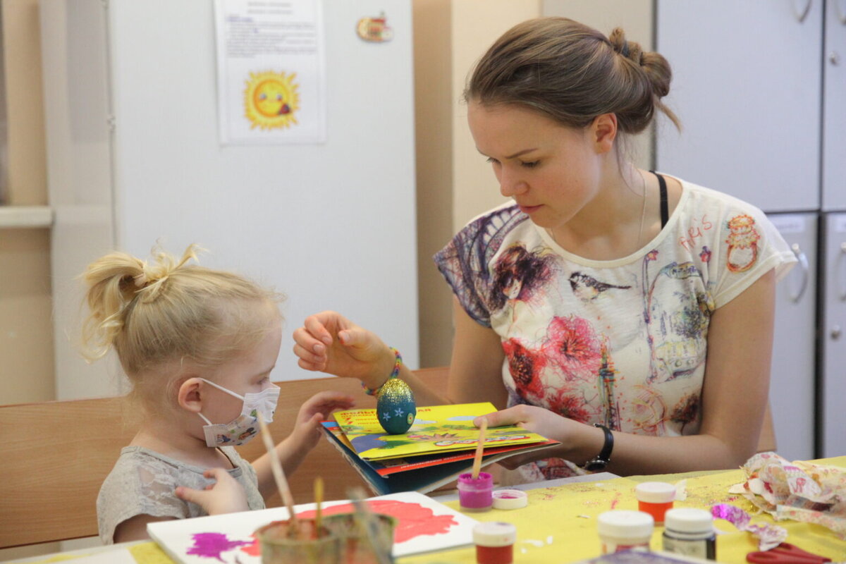 Девочка в больнице расписывает (а также посыпает блестками и какими-то звездами) пасхальное яйцо с волонтером "Даниловцев"