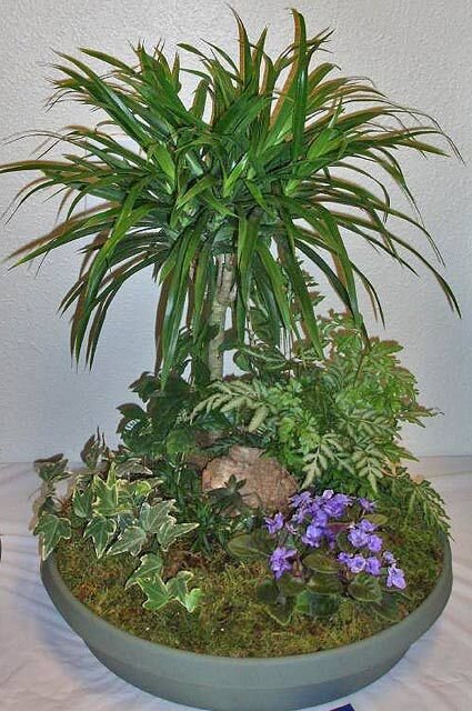 Клумбу можно создать даже в квартире. Начните с подбора ёмкости. Придумайте какой формы будет клумба. Затем добавьте в ёмкость почву. не забудьте на дно положить дренаж. Почву подберите с учетом видов растений.                                                                                   Вы можете оформить клумбу отдельными ёмкостями для  каждого растения, а можете посадить все растения в одну ёмкость. В случае общей ёмкости для всех растений подберите комнатные растения со схожими условиями произрастания. Ведь у них будет общий полив и освещенность.                                Оригинально смотрится клумба с такими растениями как бегония, хлорофитум, традесканция, плющ. Можно украсить клумбу поделками, статуэтками.  http://floraenc.ru/kustarniki-i-cvety-klumby-i-dachi/