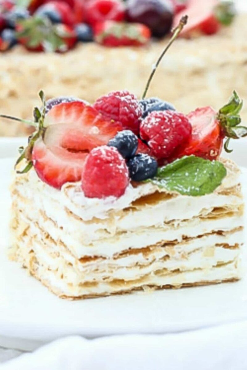 Классический торт «Наполеон»!                                                                                                                                                                                                                            Готовим хрустящие, ароматные слои теста с нежным зефирным кремом, и украшаем сверху свежими или размороженными яркими фруктами и ягодами! Рецепт восхитительного баланса вкусов между слоями теста, зефирным кремом и свежими фруктами и ягодами!                                                                                                                                           Время на подготовку: 20 минут. Время на приготовление: 25 мин. Общее время: 45 мин;
Порций: 14 порций
ИНГРЕДИЕНТЫ 
1. 450 гр  слоеного теста, размороженного
Крем:
2. 400 гр слоеного зефира
3. 4 столовые ложки несоленого сливочного масла/комнатная температура/
4. 1/4 стакана сахарной пудры
5. 1/3 стакана сгущенного молока
6. 230 гр  сливочного сыра /комнатной температуры/
7. 230 гр  размороженных или свежих ягод и фруктов для украшения торта. Вы можете использовать любые фрукты, которые есть у вас под рукой, или вашу любимую комбинацию фруктов и ягод!


ИНСТРУКЦИЯ
Разморозьте листы теста. СОВЕТ: Работайте с одним листом за раз, оставляя остальные в холодильнике.
Посыпьте столешницу мукой, макетный лист и верхнюю часть листа посыпьте мукой (чтобы было легче раскатывать лист).
Лист теста разрежьте на три полоски.
Раскатайте каждую секцию в прямоугольник размером примерно 22 см×30 см и проткните верх вилкой для равномерного выпекания.                                                      СОВЕТ: листы будут очень тонкими.
  Выпекайте около 6-8 минут, пока листы не станут золотистыми. Выпекайте по 2 листа за раз.
Повторите процесс со следующими двумя частями (оставив последние два в холодильнике). Всего у вас будет шесть слоев.
Перед сборкой полностью остудите.                                                                                                                                                                                            ПРИГОТОВИТЬ КРЕМ НАПОЛЕОН-
Взбейте сливочный сыр и масло до однородной массы.
Добавьте сгущенное молоко, сахарную пудру и слоеный крем из зефира; взбивайте на средней скорости до смешивания.
СОБРАТЬ ТОРТ
Когда слои остынут, обрежьте края, чтобы они были прямыми. Раздавите отрезанные кусочки, и отложите для декора.
Выложите первый слой на противне для торта и залейте кремом. Повторите со всеми слоями. Сверху и по бокам промажьте оставшимся кремом. Равномерно посыпьте края торта остатками крошки, посыпьте крошкой и верхние края, но оставьте середину верхнего слоя торта для укладки фруктов и ягод, иначе можно покрыть крошкой весь торт.
Добавьте свои любимые ягоды или фрукты в центр вверху.
ПРИМЕЧАНИЕ: Если вы делаете торт накануне вечером, вы можете добавить свежие фрукты и ягоды прямо перед подачей на стол. Можно слегка посыпать сахарной пудрой. Вам понравится готовить этот классический торт Наполеон! Это классный и вкусный десерт к праздничному столу!
Храните в холодильнике!