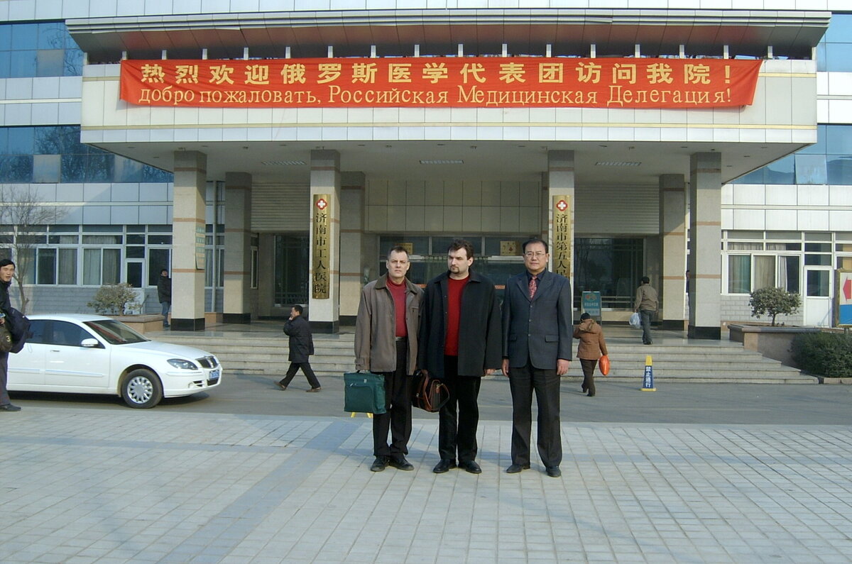 Доктор Баринов в середине, я и директор госпиталя в Цзинане, господин Ли перед входом в госпиталь под приветственным плакатом в нашу честь.