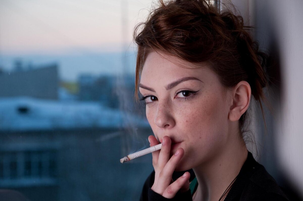 Стоковое видео категории «Премиум» — Девушка курит сигарету, глядя на сигаретный дым