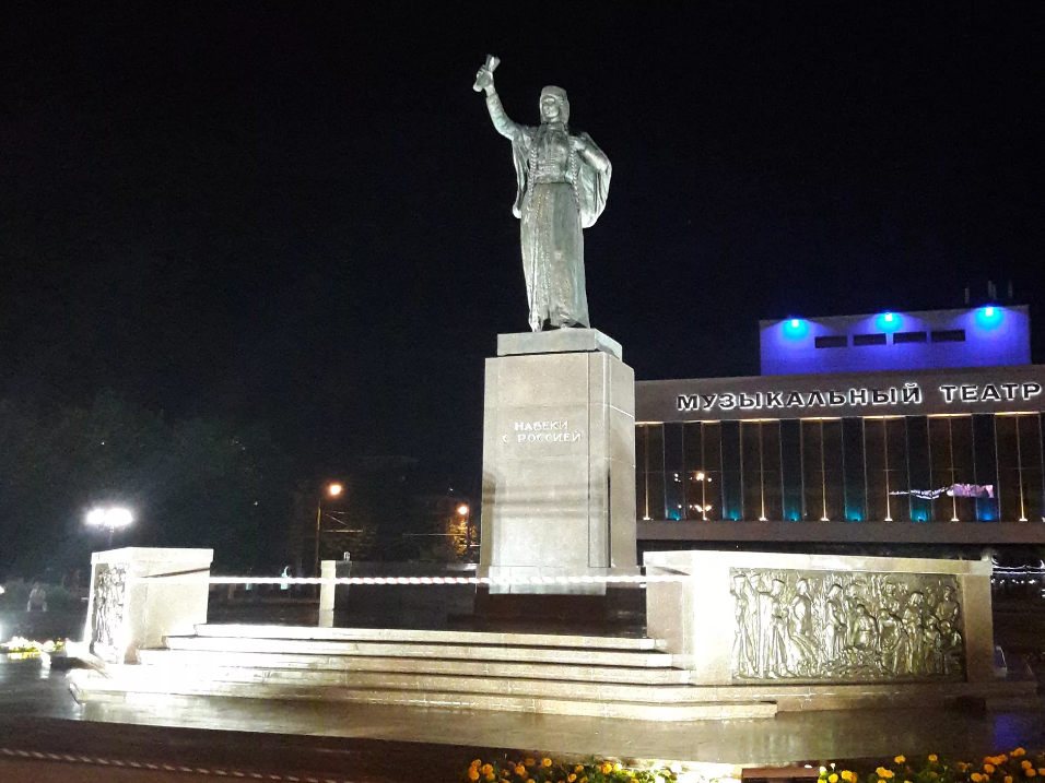 Хранительница, с улыбкой на устах, протянула вверх свернутую бумагу, словно оповещает окружающих о величайшем событии.