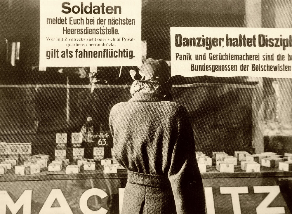 Жительница Данцига (ныне Гданьск в Польше) у витрины с объявлениями, обращенными к солдатам и местным жителям. Фотография сделана в период наступления Красной Армии на Данциг. Текст объявлений: «Солдаты, являйтесь в ближайший военный штаб. Идущие с обозами гражданского населения и околачивающиеся по частным квартирам считаются дезертирами» и «Данцигцы, соблюдайте дисциплину. Паника и распространение слухов — лучшие союзники большевиков». 1945 г.