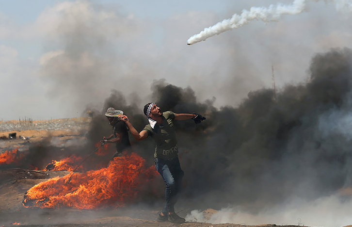 В понедельник в Иерусалиме торжественно открылось посольство США в Израиле, которое было перенесено из Тель-Авива решением президента Дональда Трампа. Что вызвало массовые протесты и столкновения, в результате которых десятки палестинцев погибли на границе сектора Газа. Как сообщают палестинские медики, по меньшей мере 60 участников протестов погибли и более 1200 человек были ранены. Ни один израильтянин при этом не пострадал. Жертвы среди палестинского населения вызваны тем, что армия Израиля применяет боевого оружия для подавления беспорядков.
Премьер-министр Израиля Биньямин Нетаньяху назвал действия военных самозащитой от радикальной группировки ХАМАС, контролирующей Газу и ставящей своей целью уничтожение Израиля.
В то же время Белый дом обвинил в столкновениях ХАМАС и заблокировал предложенный Кувейтом проект резолюции Совбеза ООН с осуждением происходящего и требованием независимого расследования столкновений.
Палестинцы возмущены этим решением, так как с их точки зрения это означает, что США признают суверенитет Израиля над всем городом, в то время как палестинцы хотят установить свою столицу в восточной части Иерусалима.
Представитель руководства Палестинской автономии Юсуф аль-Махмуд обвинил израильские власти в "ужасной резне" и попросил помощи у международного сообщества.
В свою очередь мировая общественность подвергла резкой критике применении огнестрельного оружия против демонстрантов израильскими военными. 
Правозащитная организация "Международная амнистия"(Amnesty International) осудила произошедшее, назвав обстрел демонстрантов вопиющим нарушением прав человека и международного права.
"На наших глазах происходит ужасное нарушение международного права и прав человека. Погибли люди, в том числе дети и подростки, и около двух тысяч человек получили ранения в секторе Газа. Многие сообщают о ранениях в голову и грудную клетку. Более 500 ранены боевыми патронами. Этот ужас должен немедленно прекратиться", - пишет Amnesty International в "Твиттере".
Кульминацией протестов должно было стать многомиллионное шествие из сектора Газа к разделительному сооружению на границе с еврейским государством, запланированное на 15 мая.
Жители сектора начали собираться у границы с утра, туда же были подтянуты подразделения израильской армии. Авиация армии Израиля разбрасывала листовки на границе с сектором Газа с призывом к палестинцам воздержаться от участия в насильственных акциях протеста и беспорядках. Но избежать эскалации не удалось, ожесточенные столкновения продолжились, а израильские силовики так и продолжают безнаказанно убивать палестинских демонстрантов.
