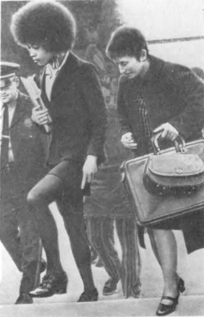 в сопровождении полицейского и своего адвоката А.Дэвис идёт на судебное заседание