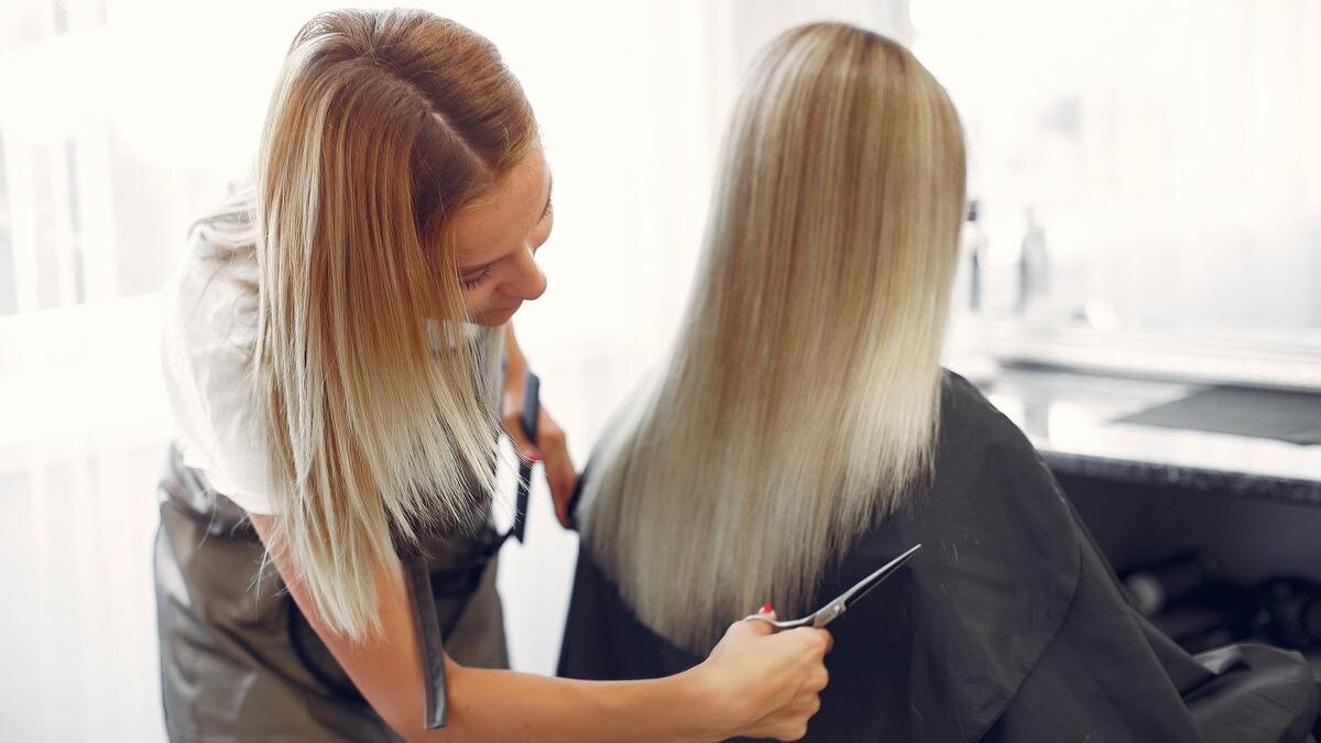    Парикмахер стрижет кончики волос блондинке:Freepik