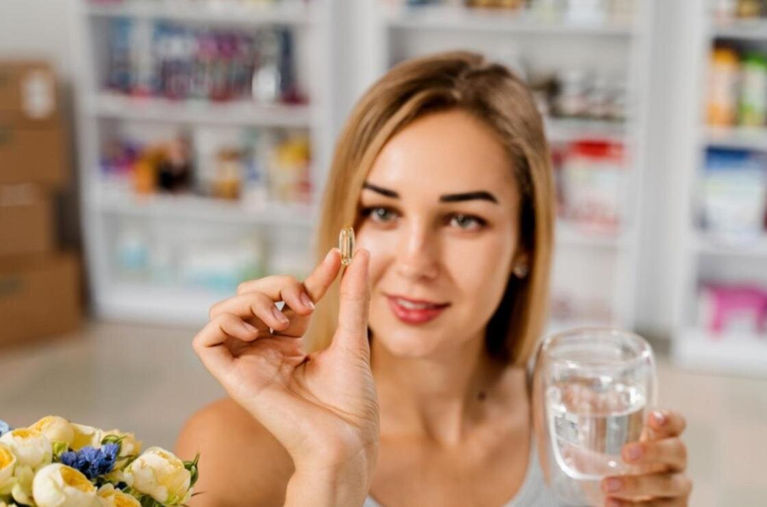    Девушка держит в руках стакан воды и капсулу витаминов:Freepik