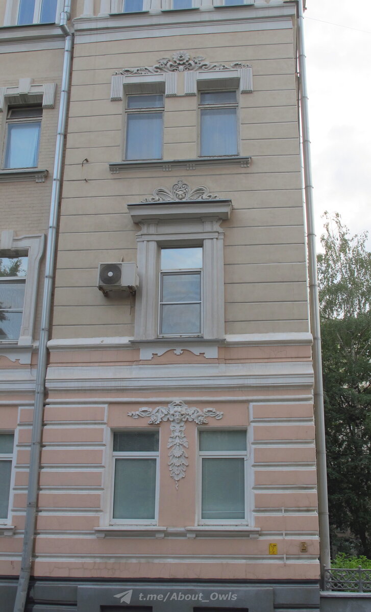 Над окном первого этажа – женская головка в цветах и фруктах, на втором этаже – сова, на третьем – цветок и листья. Фото – август 2022