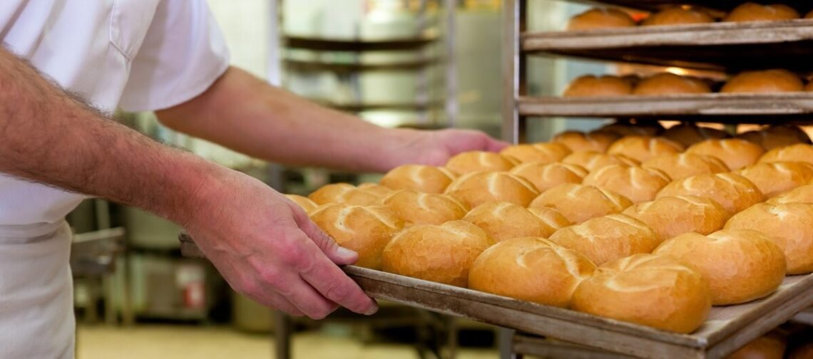    baker standing in his bakery in the morning and is baking bread or buns