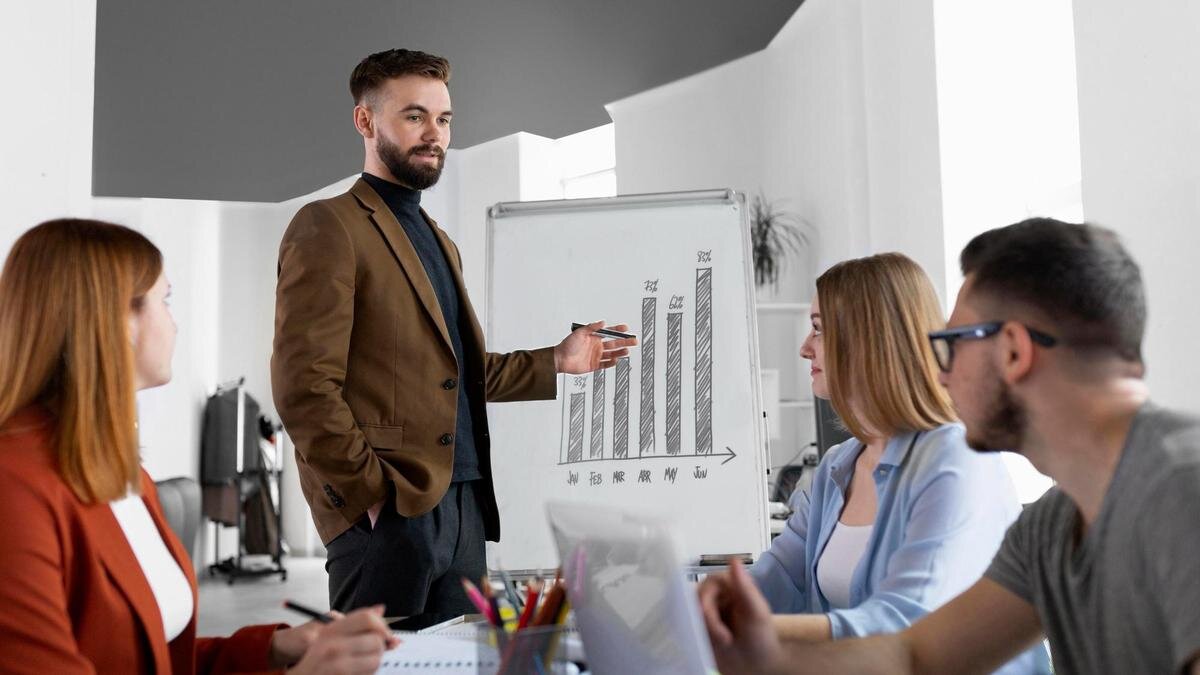    Мужчина стоит перед коллегами и указывает на график:Freepik/Freepik