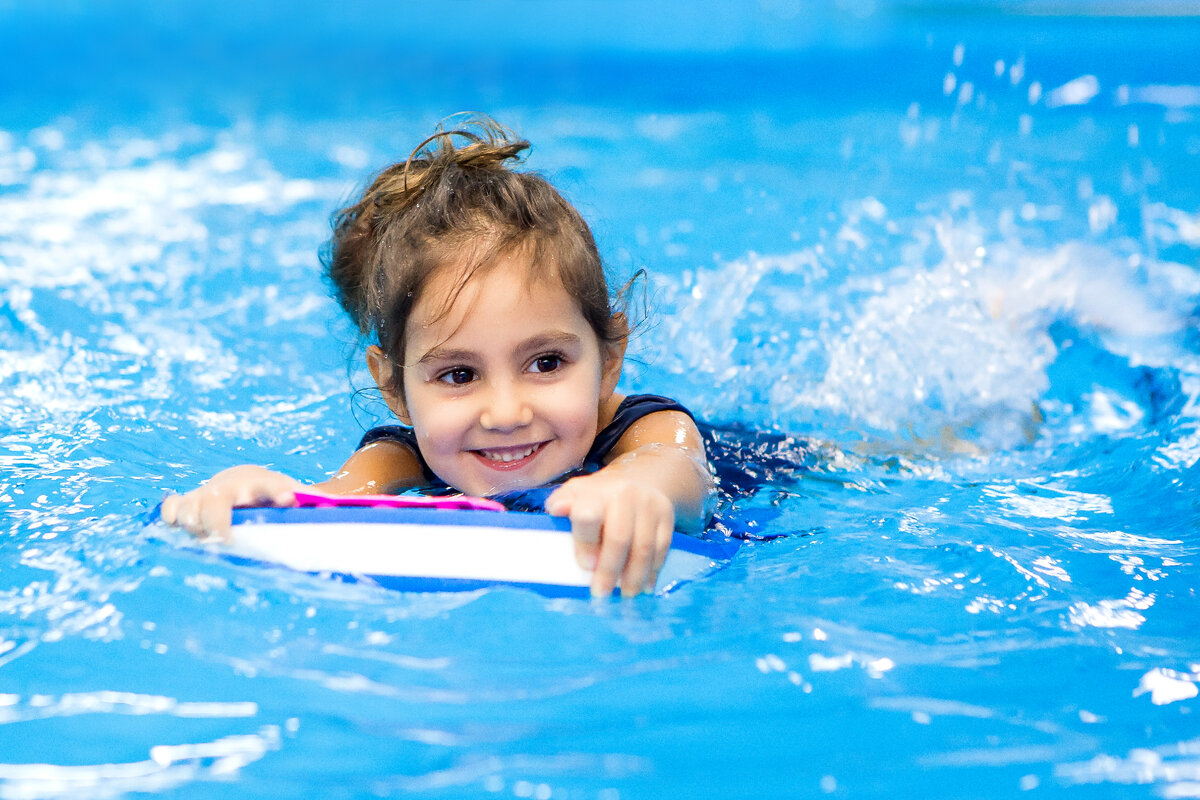 Счастливая маленькая девочка плавает в бассейне