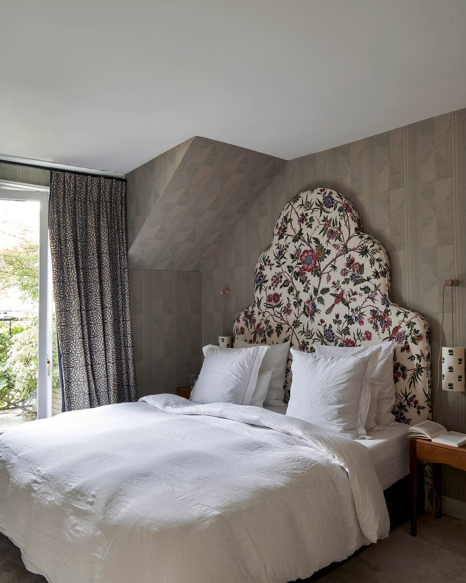 Пьер Фрей.В главной спальне тканевые шторы Sibao от Pierre Frey висят рядом с обоями бренда Indus Tise и изголовьем кровати Agathe из ткани Le Manach L'Arbre Indien. Тумбочки и бра Caneloupo выполнены в винтажном стиле .