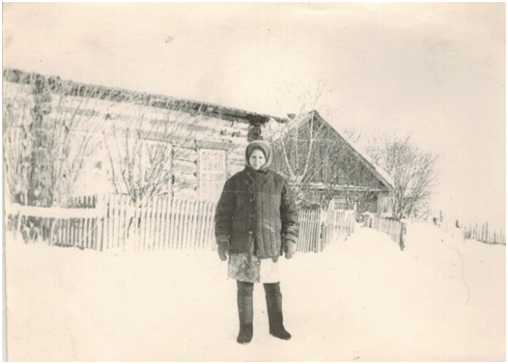 Фотография № 2. Моя мама, Домрачева Наталья Наумовна, разнорабочая участка Бельск подхоза «Решающий» стоит на проезжей части ул. Октябрьской посёлка Бельск. Стоит лицом к своему дому. Кадр от начала зимы 1972 года. Автор кадра: Домрачев В.А. Координаты нахождения фотографа: 58,1704 гр с.ш., 94,5235 гр в.д.