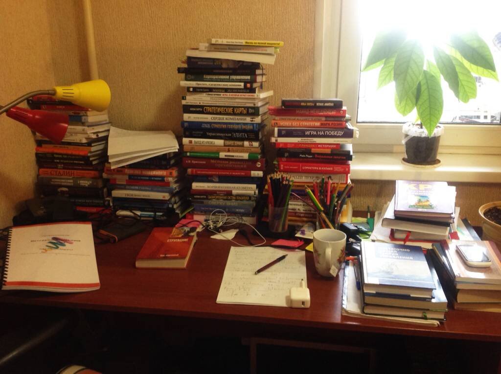 На учительском столе лежала стопка одинаковых учебников. Стол заваленный книгами. -Письменный стол заваленный книгами. Письменный стол с учебниками. Куча учебников на столе.