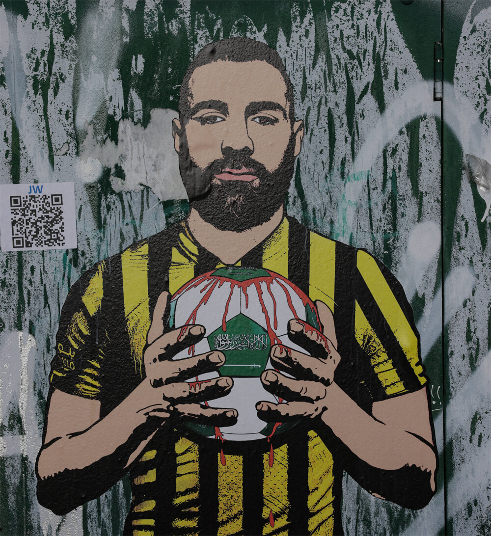    Стрит-арт художника Александро Паломбо, изображающий Карима Бензема, держащего футбольный мяч с надписью по-арабски. Фото:  www.globallookpress.com/ IMAGO/Jonathan Moscrop