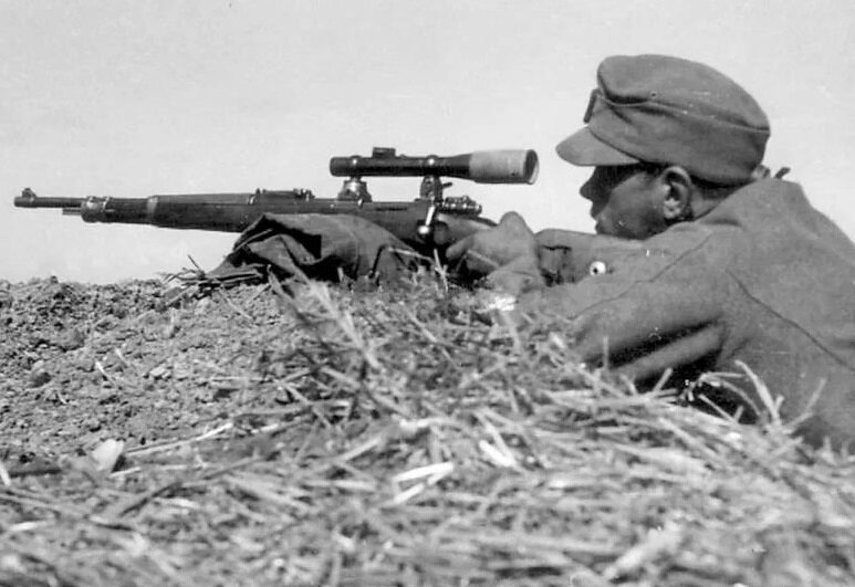 Немецкий снайпер в позиции лёжа целится из снайперской винтовки.