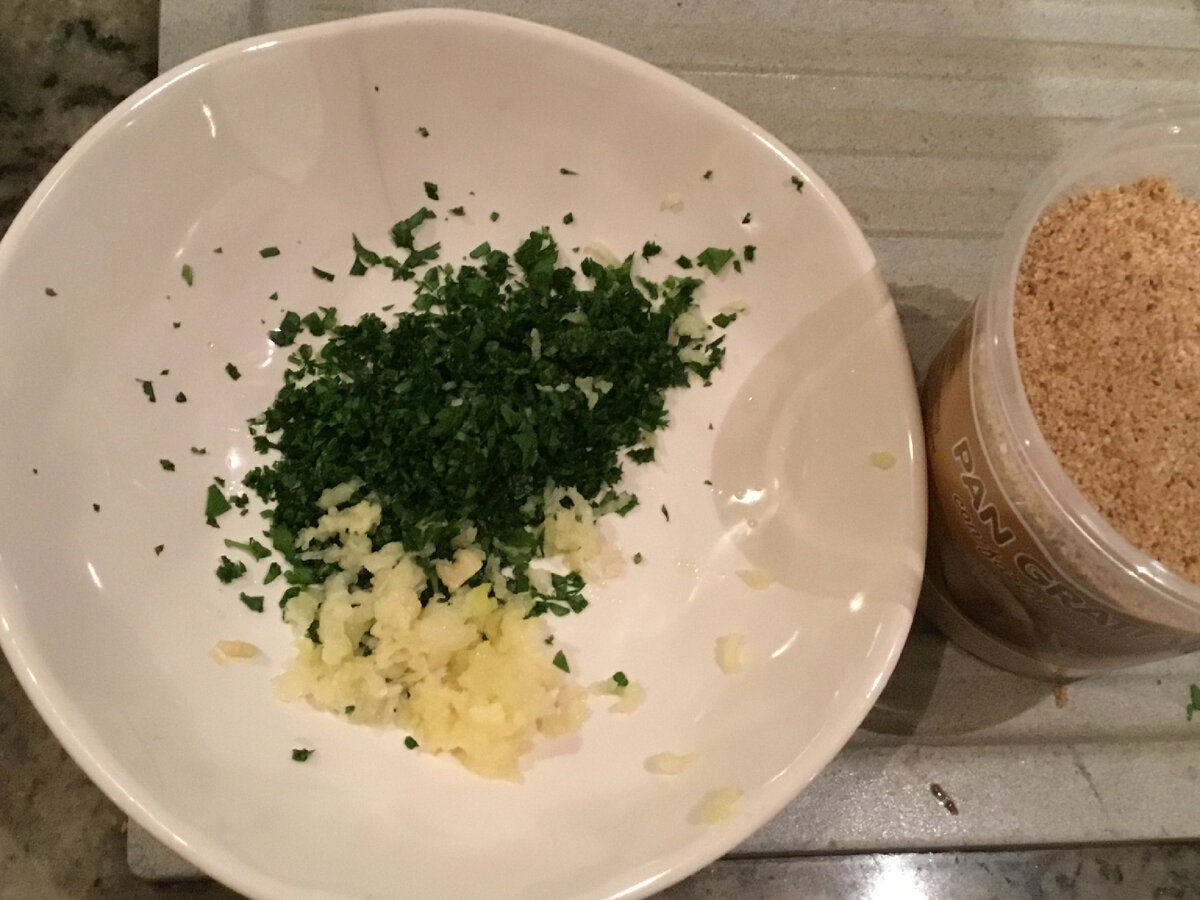 Пропустим через пресс пару зубчиков чеснока и выложим вместе с петрушкой в миску или глубокую тарелку. Добавим панировочных сухарей. 